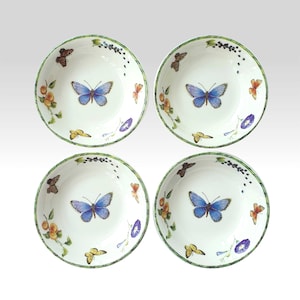 Può includere: Quattro ciotole in ceramica bianca con un design a farfalle e fiori. Ogni ciotola presenta una farfalla blu centrale, circondata da farfalle più piccole, fiori e un bordo verde. Le ciotole sono decorate con una varietà di colori.