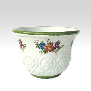 Könnte beinhalten: Weißer Keramik-Blumentopf mit grünem Rand und Boden, verziert mit bunten Blumenmustern. Der Topf hat ein strukturiertes Design mit sich wiederholenden Engelsgesichtern. Ein dekoratives Element für den Innen- oder Außenbereich.