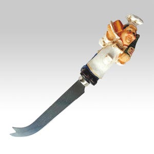 Peut inclure: Un couteau à fromage décoratif avec une figurine de chef souriant tenant une bouteille et du pain. Le couteau a une lame en acier inoxydable avec une pointe incurvée. Le chef porte un uniforme blanc et un chapeau de chef.