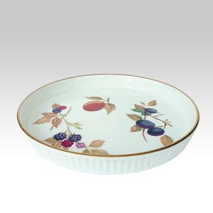 Może przedstawiać: Biała ceramiczna forma do ciasta z karbowanym brzegiem i złotą obwódką. Wnętrze zdobi kolorowy wzór owoców ze śliwkami, jeżynami i liśćmi. Idealna do pieczenia i serwowania ciast.