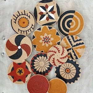 Puede incluir: Un conjunto de 11 piezas redondas de decoraci&oacute;n de pared hechas de cuerda trenzada con varios patrones geom&eacute;tricos y florales en negro, marr&oacute;n, rojo y blanco.