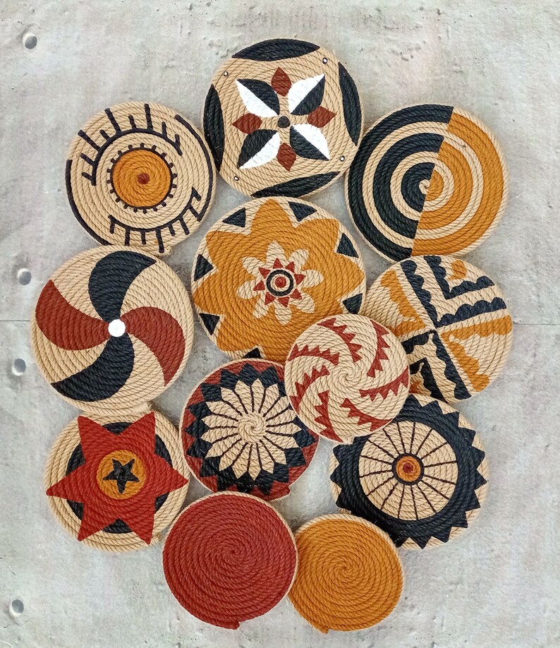 Puede incluir: Un conjunto de 11 piezas redondas de decoraci&oacute;n de pared hechas de cuerda trenzada con varios patrones geom&eacute;tricos y florales en negro, marr&oacute;n, rojo y blanco.