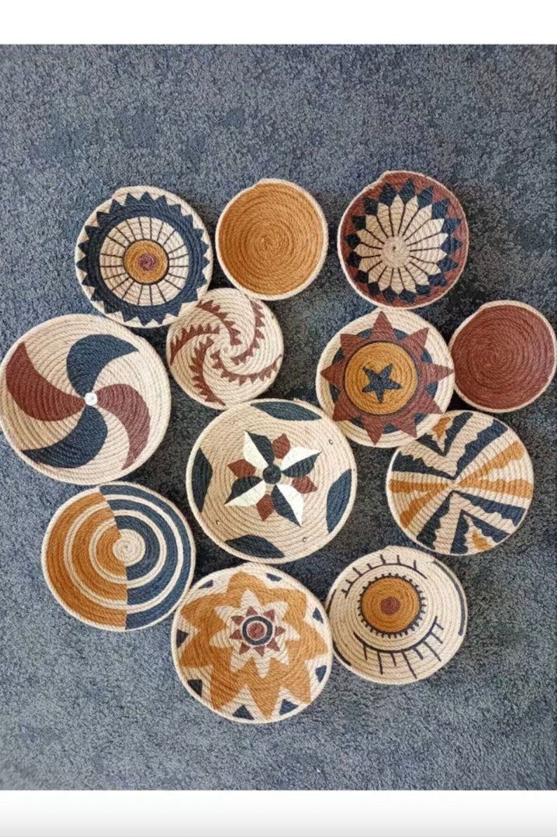 Puede incluir: Una colecci&oacute;n de 12 piezas redondas de decoraci&oacute;n de pared tejidas en varios patrones geom&eacute;tricos. Las piezas est&aacute;n hechas de materiales naturales y presentan una combinaci&oacute;n de colores marr&oacute;n, negro y blanco.