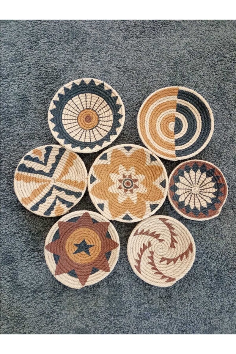 Puede incluir: Siete piezas redondas de decoraci&oacute;n de pared tejidas con diferentes patrones geom&eacute;tricos en negro, marr&oacute;n y beige.