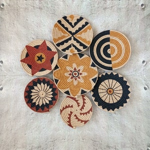 Puede incluir: Conjunto de siete piezas de decoraci&oacute;n de pared tejidas en varios patrones geom&eacute;tricos. Las piezas est&aacute;n hechas de materiales naturales y presentan una combinaci&oacute;n de colores negro, marr&oacute;n y beige.