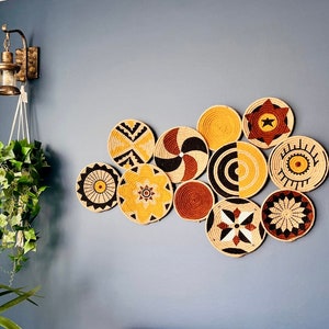 Puede incluir: Una colecci&oacute;n de 10 piezas redondas de decoraci&oacute;n de pared tejidas en varios patrones y colores, incluyendo negro, blanco, amarillo y marr&oacute;n. Las piezas est&aacute;n dispuestas en forma de nube en una pared azul.