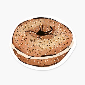May include: A round, golden-brown bagel with a textured surface covered in small, dark brown and tan seeds. The bagel is sliced horizontally through the middle, revealing a smooth, light cream-colored layer of filling between the two halves.