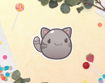 Könnte beinhalten: Eine graue Comic-Katze mit rosa Ohren und einem weißen Streifen auf dem Bauch. Die Katze lächelt und hat große, runde Augen. Die Katze befindet sich auf einem hellgelben Hintergrund mit Konfetti.