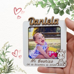 Può includere: Una cornice bianca con una foto di un bambino sorridente. Il nome "Daniela" è in lettere di legno sopra la foto. Il testo "Mi Bautizo 06 de Diciembre de 2026" è sotto. Un'illustrazione di giraffa è sul lato destro.