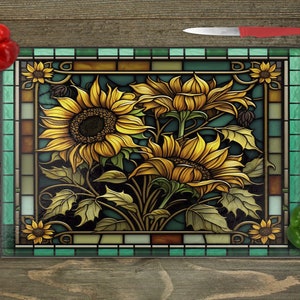 May include: A stained glass style cutting board with a design of sunflowers in shades of yellow, brown, and green. The board has a teal border.