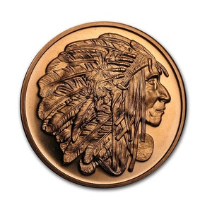 Pode incluir: Uma moeda redonda de cor dourada com o perfil de uma pessoa indígena usando um cocar com penas. A moeda tem um design em relevo e uma borda lisa.