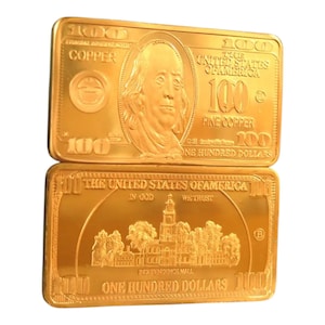 May include: Two gold-coloured rectangular bars, each resembling a £100 bill. The top bar features an image of Benjamin Franklin and the text "COPPER" and "ONE HUNDRED DOLLARS." The bottom bar displays Independence Hall and the text "THE UNITED STATES OF AMERICA."