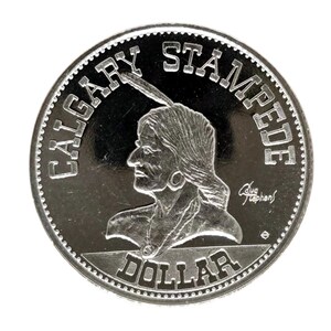 May include: A silver Calgary Stampede dollar coin. The coin features a profile of a Native American person wearing a feather headdress. The words "CALGARY STAMPEDE" and "DOLLAR" are inscribed on the coin.