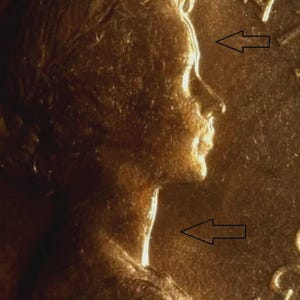 May include: A close-up of a gold-coloured coin showing a profile of a person. The coin's surface has a textured appearance, with details of the face and hair visible. The coin's edge is slightly visible, and the overall design is classic.