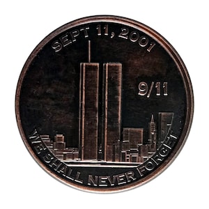May include: A bronze-colored commemorative coin. The coin features the Twin Towers, the date "SEPT 11, 2001", and the text "9/11". The words "WE SHALL NEVER FORGET" are inscribed around the bottom edge of the coin. The coin has a detailed cityscape.