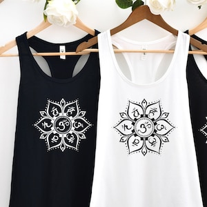 May include: Three tank tops with a white mandala design featuring the Om symbol and other Sanskrit characters. The tank tops are black and white.