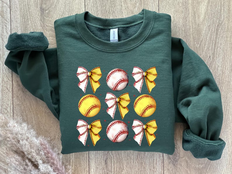 May include: A dark green sweatshirt featuring a design of yellow and white bows and baseballs. The baseballs are yellow with red stitching.
