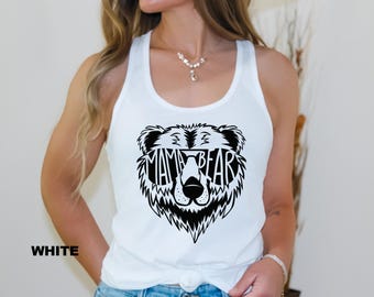 May include: White tank top with a black graphic of a bear's face wearing sunglasses, with the words "MAMA BEAR" in the center. The word "WHITE" is printed in black on the bottom left of the image. The top is a racerback style.