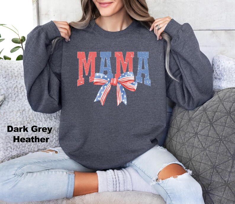 Pu&ograve; includere: Felpa color grigio scuro melange con la parola "MAMA" in lettere rosso, bianco e blu e un fiocco rosso, bianco e blu.