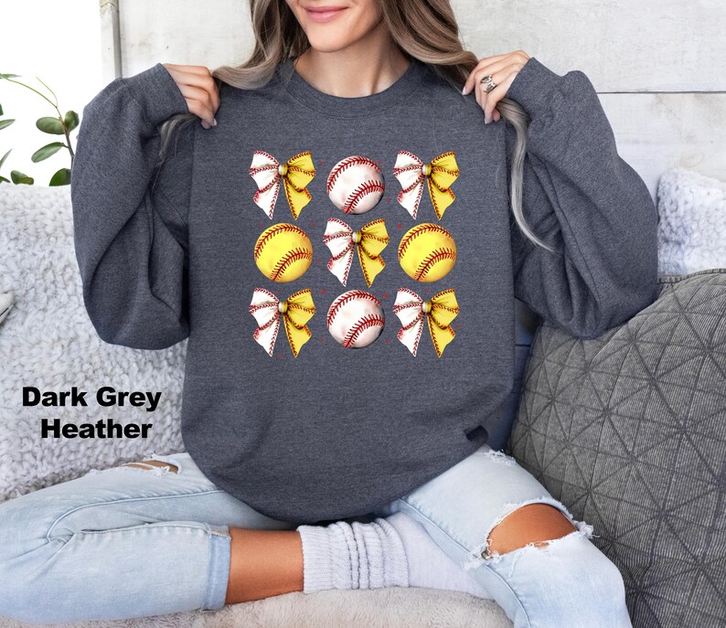 May include: Dark grey heather sweatshirt with a graphic of six yellow and white softball with yellow bows on a dark grey background.