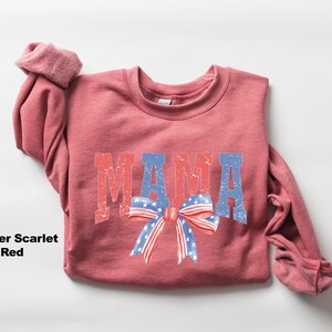 Pu&ograve; includere: Una felpa di colore rosso scarlatto melange con la parola "MAMA" stampata in rosso, bianco e blu con un fiocco rosso, bianco e blu.