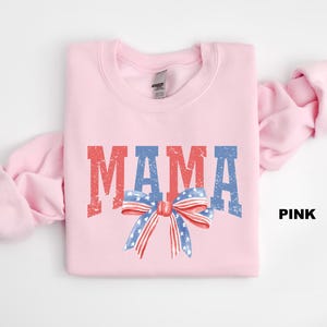 Pu&ograve; includere: Felpa rosa con la parola "MAMA" in lettere rosso, bianco e blu con un fiocco rosso, bianco e blu con stelle.