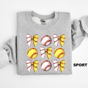 May include: A grey sweatshirt with a design of yellow and white softball bows and baseballs. The text "SPORT GREY" is in the bottom right corner of the image.