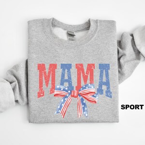 Pu&ograve; includere: Una felpa grigia con la parola "MAMA" in lettere rosse e blu con un fiocco rosso, bianco e blu. La felpa &egrave; disponibile in grigio sportivo.