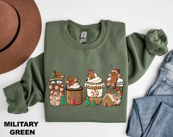 May include: A green sweatshirt with a Christmas-themed design featuring gingerbread men and women sitting on top of mugs of hot chocolate, coffee, and peppermint hot chocolate. The design includes a gingerbread house and candy canes.
