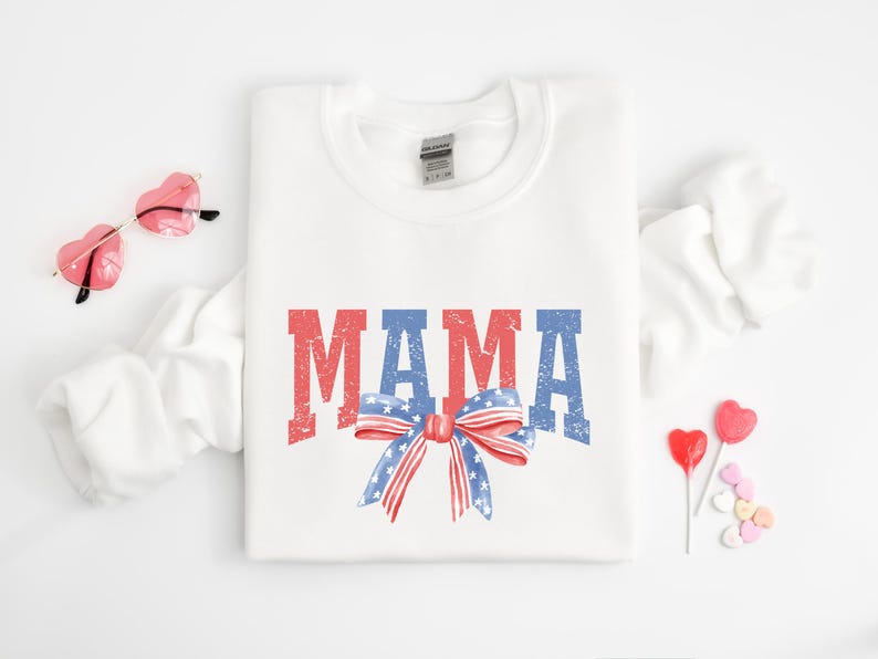 Pu&ograve; includere: Felpa bianca con la parola "MAMA" in lettere rosso, bianco e blu con un fiocco rosso, bianco e blu con stelle.