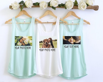 May include: Three tank tops in mint green and white hang on wooden hangers. Each tank top has a rectangular image with the text "YOUR PHOTO HERE" or "YOUR TEXT HERE". A floral arrangement of white roses sits above the tank tops.