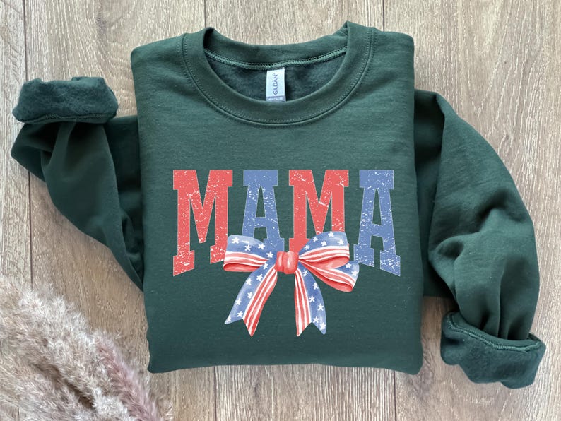 Pu&ograve; includere: Una felpa verde scuro con la parola "MAMA" stampata in rosso, bianco e blu con un fiocco rosso, bianco e blu.