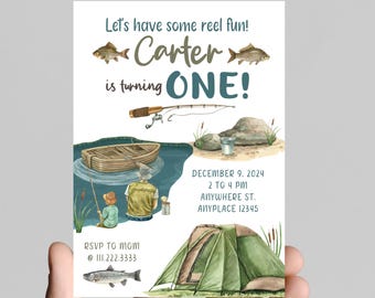 May include: A fishing-themed first birthday party invitation with a watercolor illustration of a lake, a boat, a fishing rod, a tent, and two fish. The text reads "Let's have some reel fun! Carter is turning ONE!" and includes the date, time, and location of the party. RSVP information is also included.