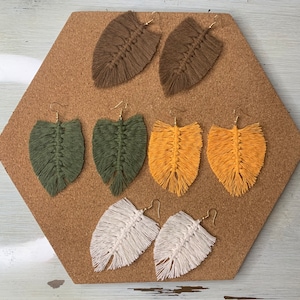 May include: A set of six handmade feather earrings in various colors, including brown, green, yellow, and white. The earrings are made with macrame and have a tassel design.