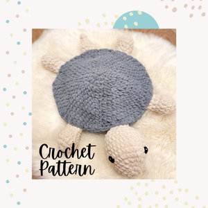 May include: Crochet pattern for a grey and white turtle amigurumi. The turtle is lying on a white fluffy surface. The text "Crochet Pattern" is written below the turtle.
