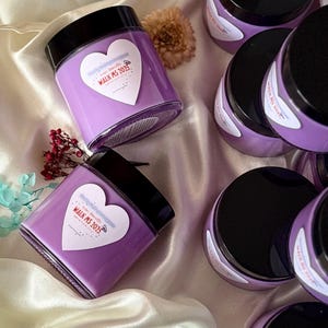 May include: Several lavender-colored jars with black lids are arranged on a satin surface. Each jar has a heart-shaped label with the text "Walk MS 2025". Decorative flowers are scattered around the jars.