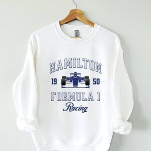 Peut inclure: Sweat-shirt blanc avec un graphique bleu d'une voiture de course et le texte "HAMILTON 19 50 FORMULA 1 Racing".