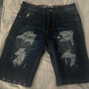 May include: Dark blue denim shorts with multiple distressed areas and frayed edges. The shorts have a straight leg and a relaxed fit.