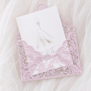 Könnte beinhalten: Ein helllavendelfarbener Spitzenumschlag mit einer weißen Karte. Die Karte zeigt eine Aquarellillustration eines Kleides und den Text Thank You in eleganter Schrift. Der Umschlag hat eine spitze Klappe mit floralen Spitzendetails.