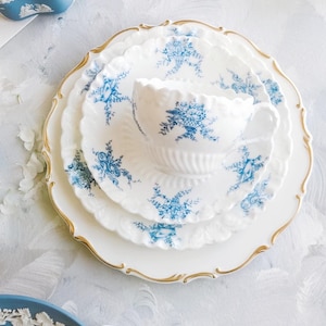 May include: A white teacup and saucer set with blue floral patterns and gold trim, arranged on a white plate. The set is part of a larger collection of fine china, with additional plates and a blue decorative box visible.