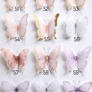 May include: A collection of twelve butterfly stickers arranged in a grid, labelled with numbers 51 through 62. The stickers feature various shades of pink, purple, and white, with some designs incorporating gold foil accents on the wings.