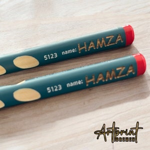 K&ouml;nnte beinhalten: Zwei t&uuml;rkisfarbene Bleistifte mit roten Enden und goldener Beschriftung. Die Stifte sind mit "5123 name: HAMZA" beschriftet.