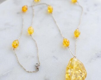 May include: A delicate silver-toned chain necklace featuring several small, faceted yellow beads spaced along the length and a single, larger, irregular-shaped yellow pendant at the center. The necklace includes a small metal lobster claw clasp.