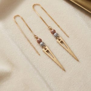 May include: A pair of gold-tone threader earrings featuring a delicate box chain. Each earring is accented with one textured rose gold-tone bead and one textured silver-tone bead, terminating in a long, slender, triangular gold-tone pendant.