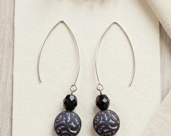 May include: A pair of silver-toned V-shaped ear wires featuring dangling beads. Each earring has a small, faceted black bead positioned above a larger, round, dark-colored disc bead with an embossed, iridescent swirling pattern on its surface.