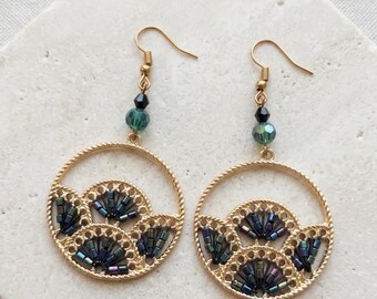 May include: A pair of gold-toned hoop earrings featuring a textured circular frame with three fan-shaped cutouts filled with iridescent dark blue and purple bugle beads. Each earring hangs from a gold hook with a small black and teal bead accent.