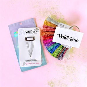 Peut inclure: Un brin de cheveux argenté à clipser avec un pompon de paillettes arc-en-ciel. L'emballage porte le texte "WildMane Clip-in Hair Tinsel" et "sparkle in a snap!"