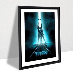 以下が含まれることがあります： 青と黒のTron: Legacyの映画ポスターのデザインが施された額装されたポスター。ポスターには、青い光の中で立っている2人の人物が描かれており、下部に「TRON LEGACY」の文字が書かれている。