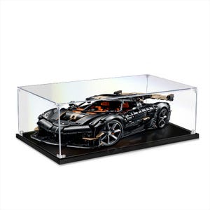May include: A black and orange model sports car constructed from building blocks, displayed inside a clear rectangular acrylic protective case with a solid black base. The vehicle features detailed wheels, a rear spoiler, and an open cockpit design.