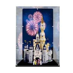 May include: A clear acrylic display case containing a large, multi-level toy castle model with blue and white towers, gold accents, and small character figures at the entrance, set against a dark blue background featuring pink fireworks.